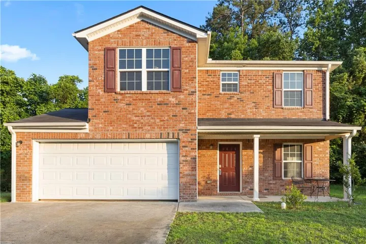 Brick facade residence featuring a covered front porch, an attached garage, and contrasting window shutters