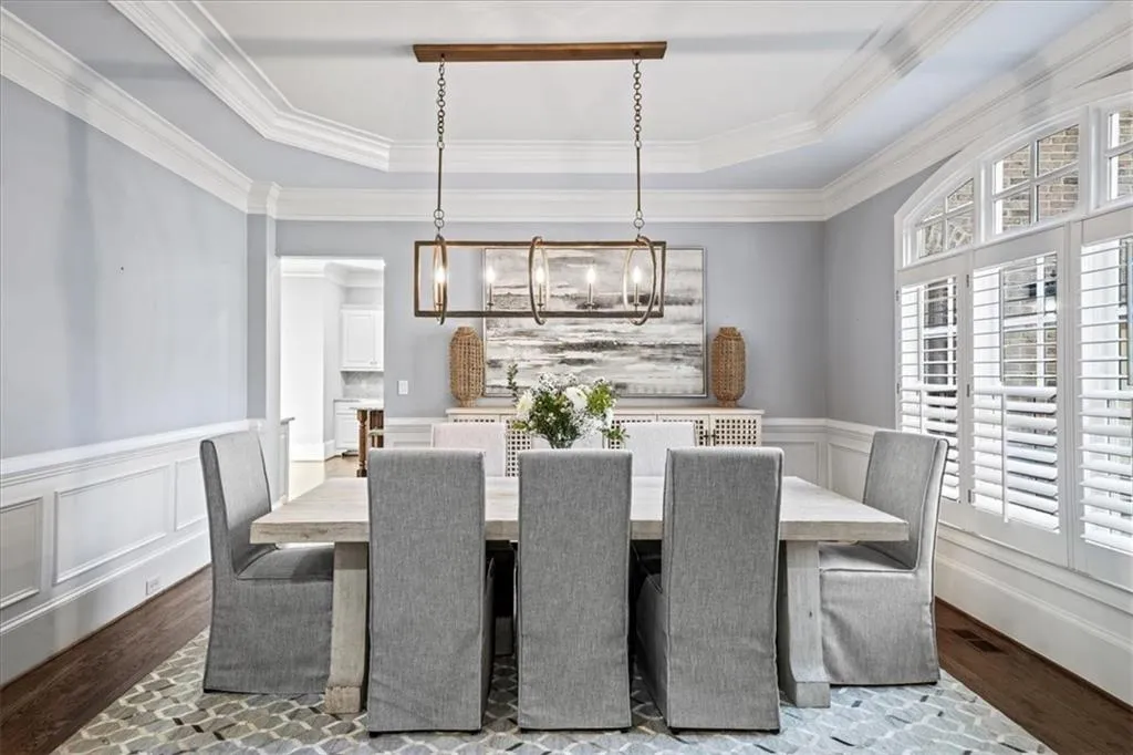 Dining room with a raised ceiling, wainscoting, dark wood-style floors, a decorative wall, and ornamental molding