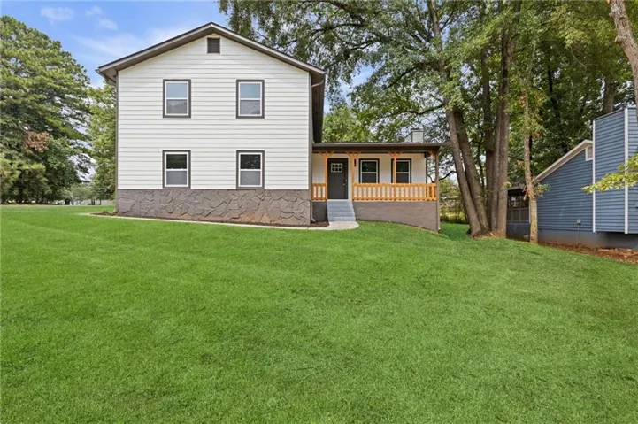 White exterior siding with a stone-finish foundation, covered front porch, light wood-tone railings, and a wide grassy lawn