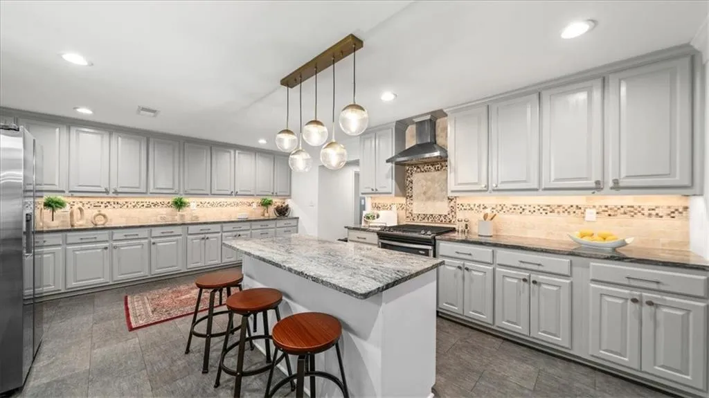 Kitchen features include an island, decorative light fixtures, range hood, a kitchen bar, and gas range with ventilation.
