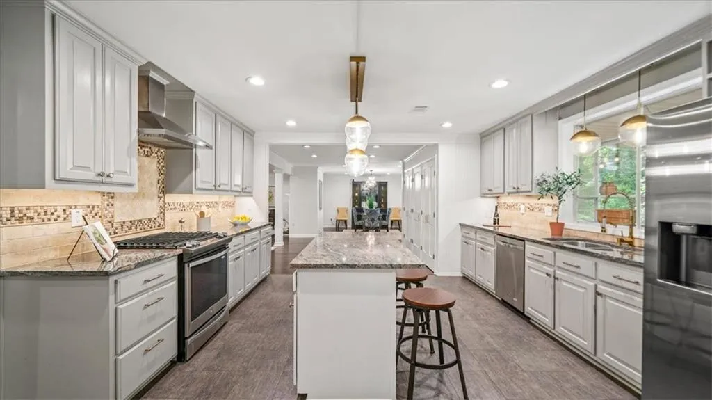 Kitchen features include light stone counters, a kitchen island, hanging light fixtures, appliances with stainless steel finishes, under cabinet lighting, and backsplash