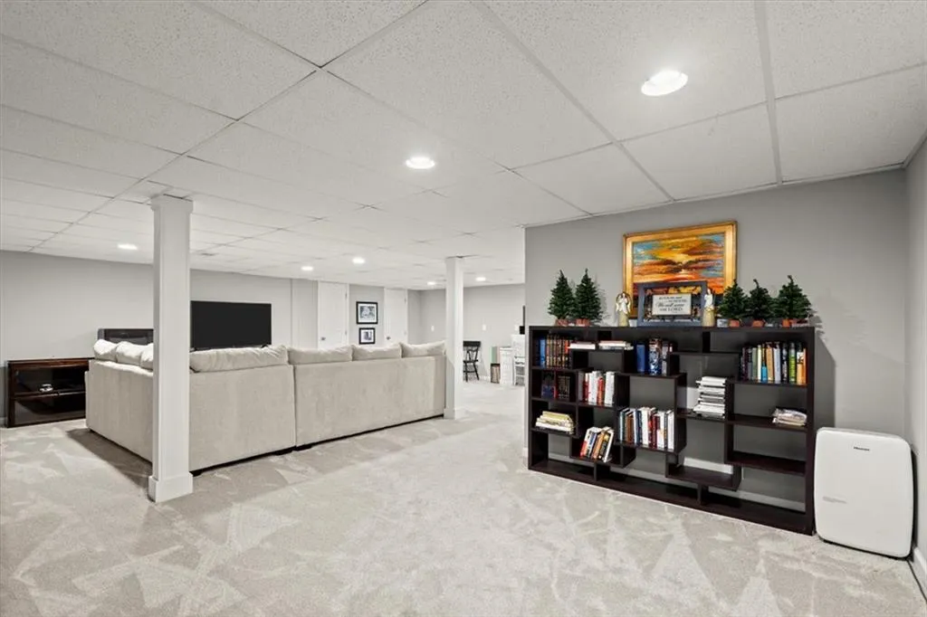 full, finished basement living room featuring decorative columns, new carpet, additional lighting.