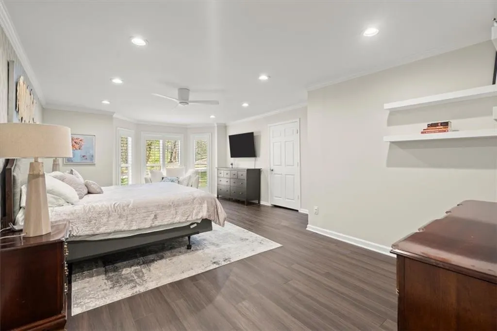 Owner's suite bedroom on main level featuring ornamental molding, hardwood flooring, ceiling fan and recessed lighting.
