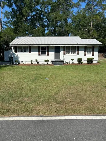 White exterior with a metal roof, front door with storm door, and decorative window shutters