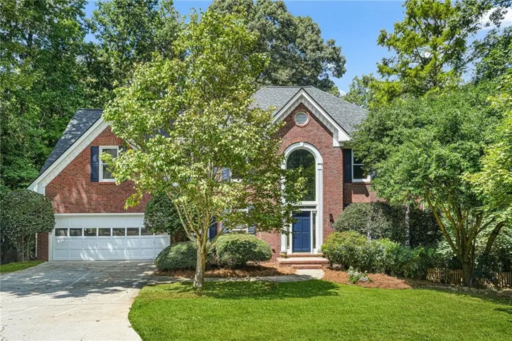 Brick exterior, arched window, dark blue entry door, two-car garage, and established landscaping