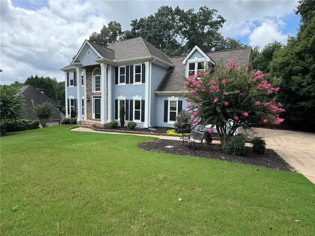 Two-story stucco home featuring a brick facade accent, a gabled roofline, and dormer windows