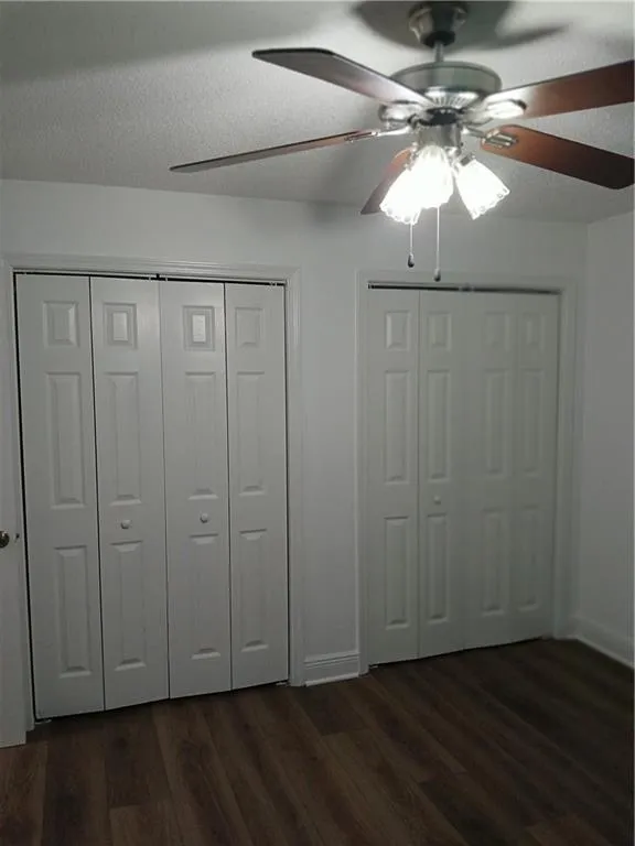 Unfurnished bedroom featuring dark wood-style flooring, multiple closets, a textured ceiling, and a ceiling fan