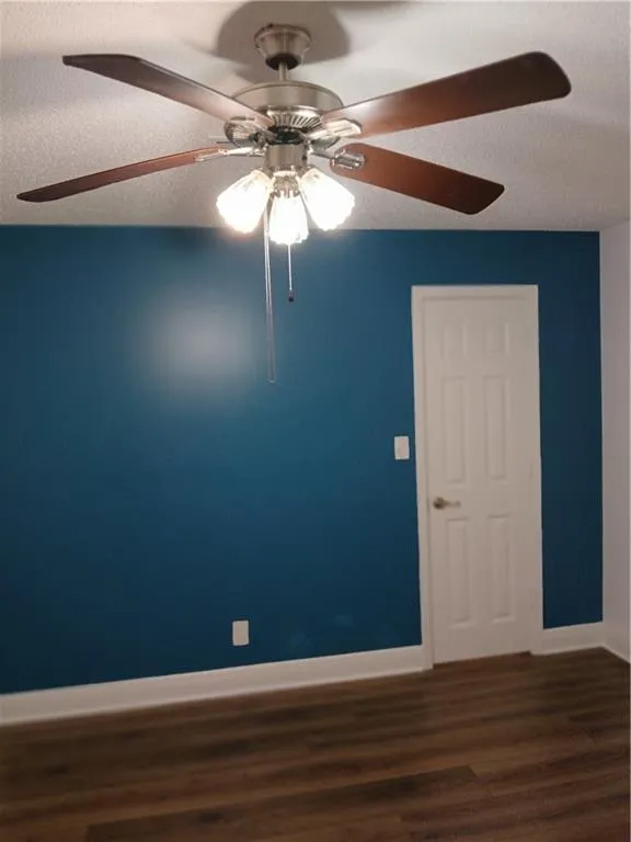 Empty room featuring dark wood-style flooring, a textured ceiling, and ceiling fan