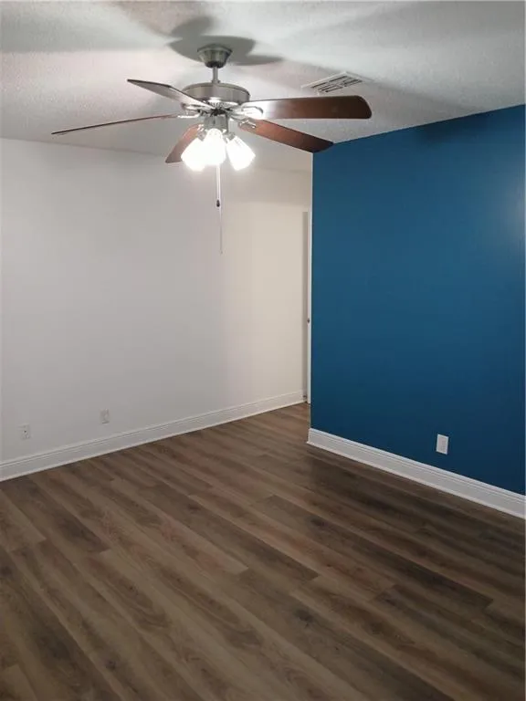 Unfurnished room with dark wood-style floors, a textured ceiling, and ceiling fan
