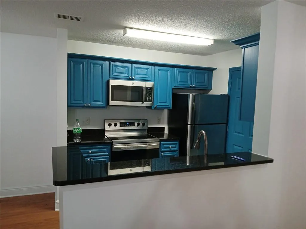 Kitchen with stainless steel appliances, blue cabinetry, wood finished floors, dark stone counters, and a peninsula
