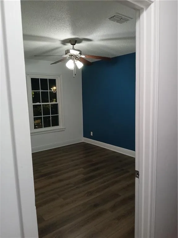 Unfurnished room with dark wood finished floors, a textured ceiling, and a ceiling fan
