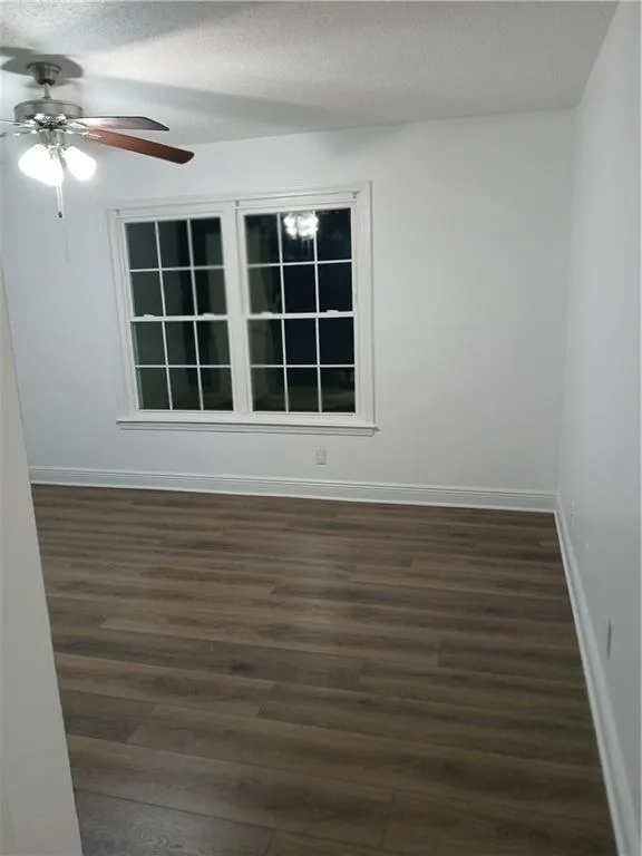 Spare room with dark wood-style floors, a textured ceiling, and a ceiling fan