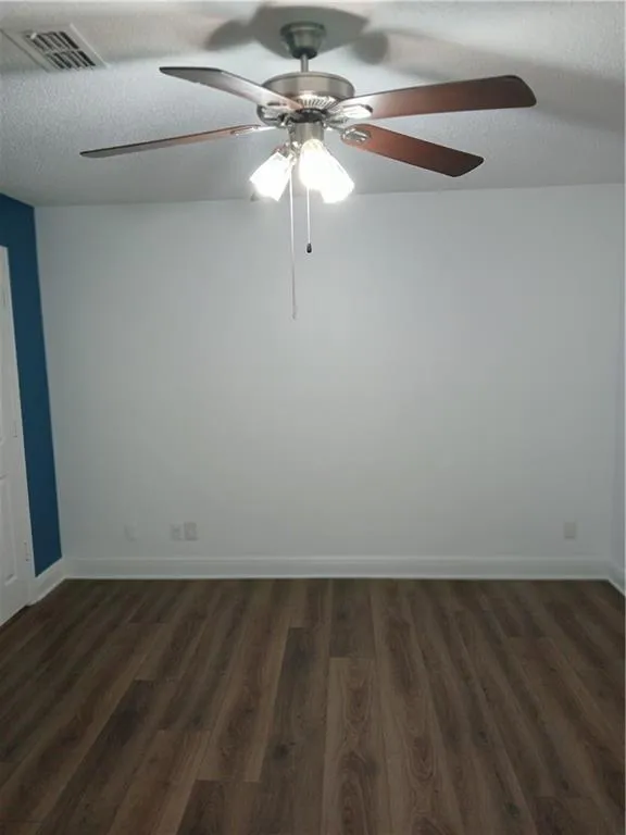 Unfurnished room with dark wood-style flooring, ceiling fan, and a textured ceiling