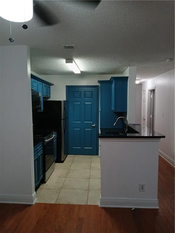 Kitchen featuring blue cabinetry, stove, light wood-type flooring, a textured ceiling, and a peninsula
