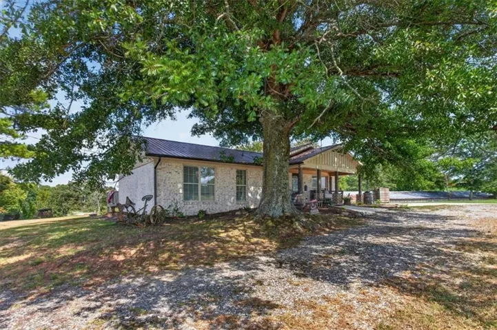 White brick exterior with a dark metal roof, featuring a covered front porch and mature trees
