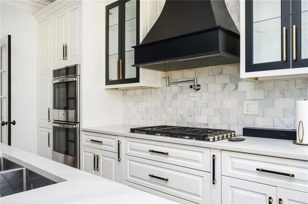 Kitchen featuring crown molding, decorative backsplash, custom range hood, appliances with stainless steel finishes, and white cabinetry