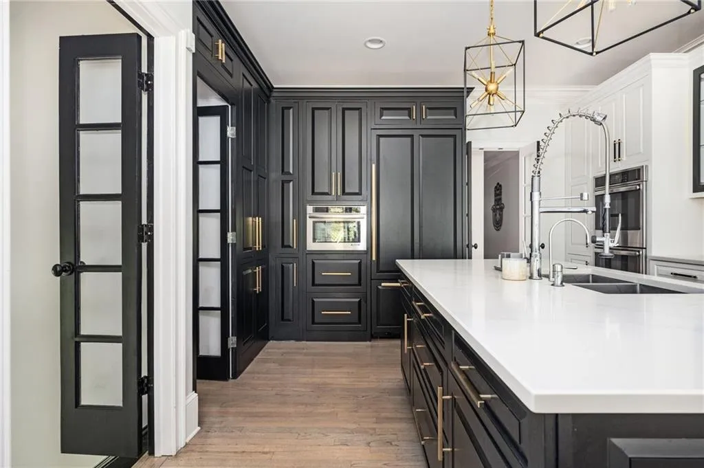 Kitchen featuring a kitchen island with sink, sink, hardwood / wood-style flooring, decorative light fixtures, and stainless steel double oven