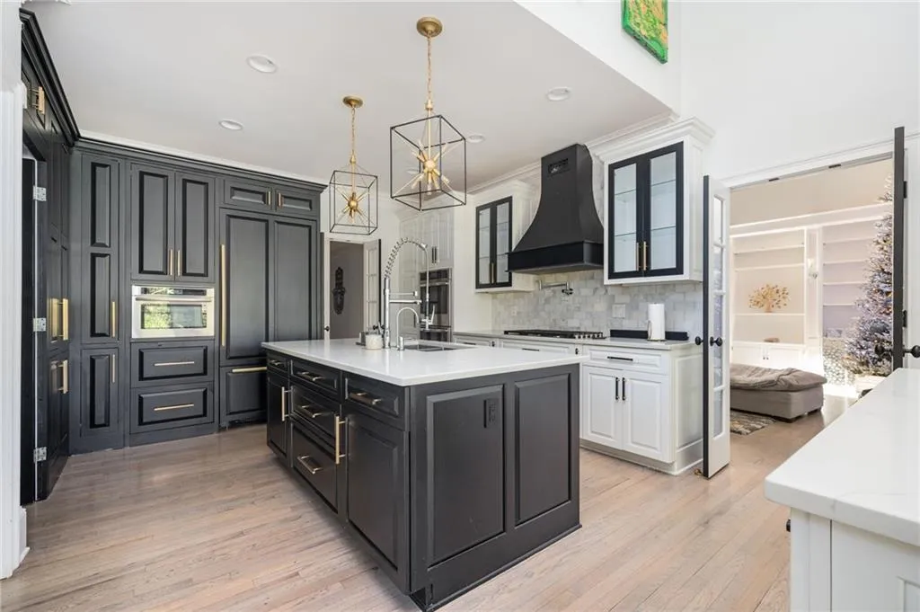 Kitchen with custom exhaust hood, a kitchen island with sink, pendant lighting, light hardwood / wood-style flooring, and white cabinetry