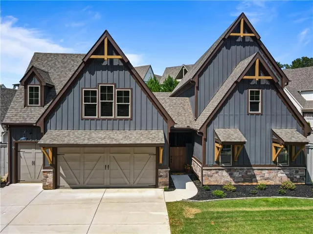 Charcoal board-and-batten siding with dark trim, stone veneer accents, multiple gable rooflines, two garage doors, and a concrete driveway