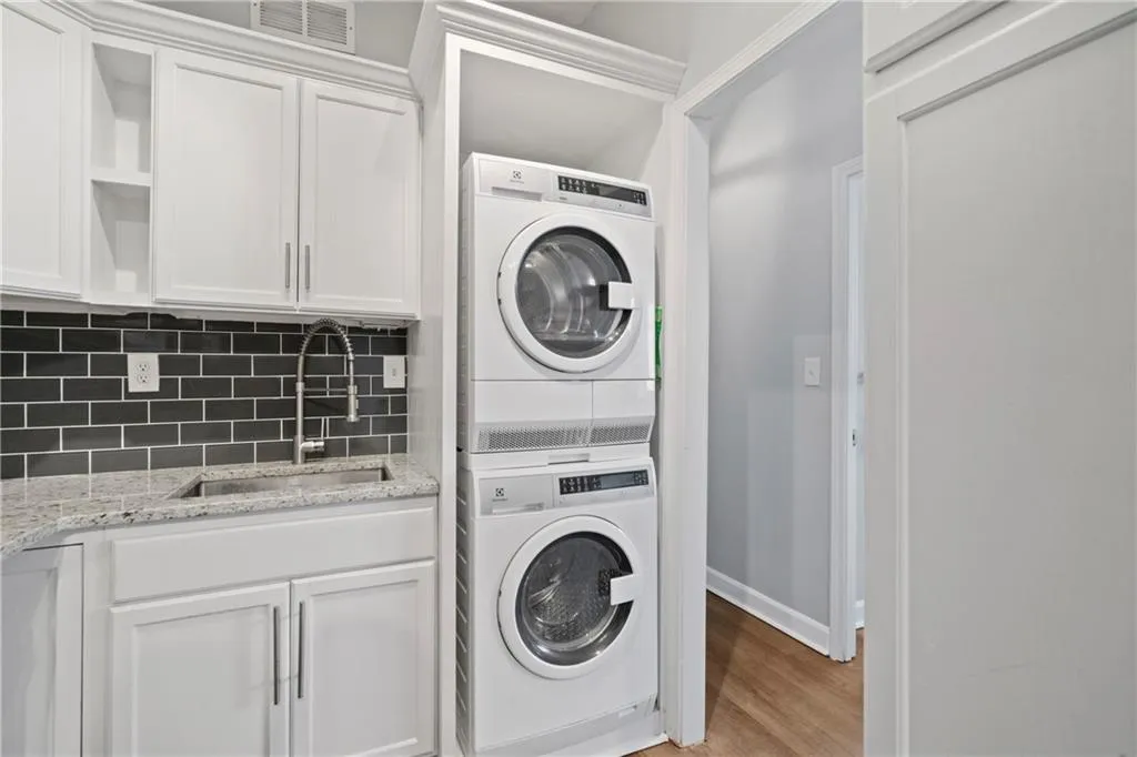Washroom featuring light hardwood / wood-style floors, stacked washer / drying machine, and sink