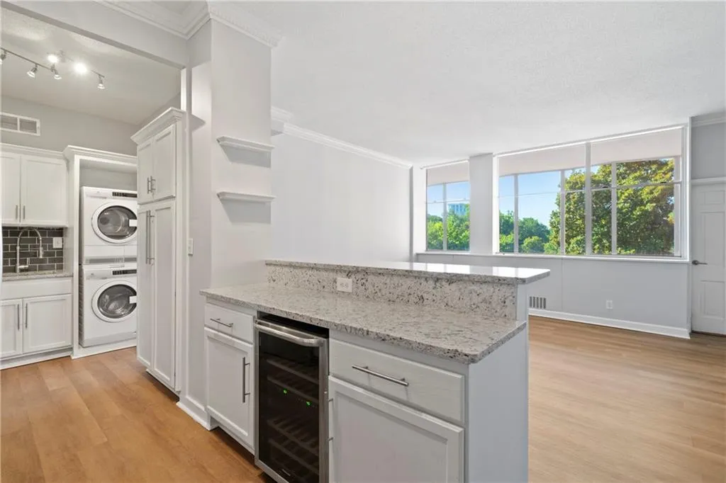 Kitchen with white cabinetry, wine cooler, light stone countertops, stacked washer / dryer, and light wood-type flooring