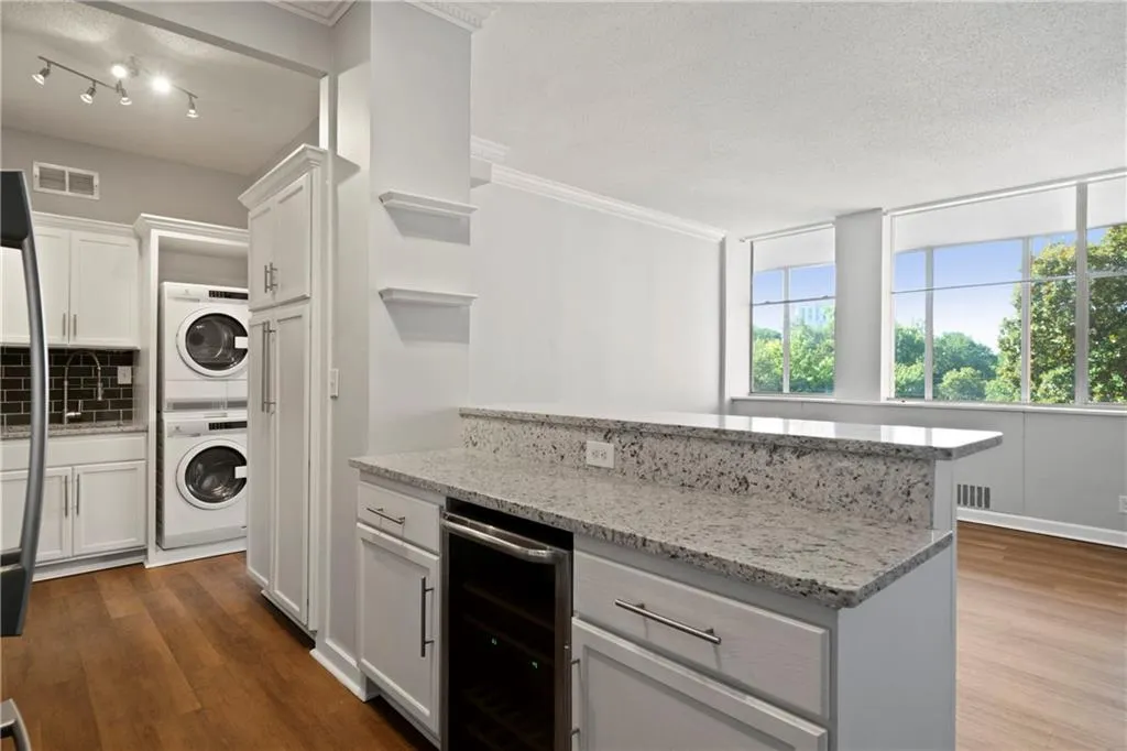 Kitchen featuring light stone counters, dark hardwood / wood-style floors, beverage cooler, white cabinetry, and stacked washer and clothes dryer