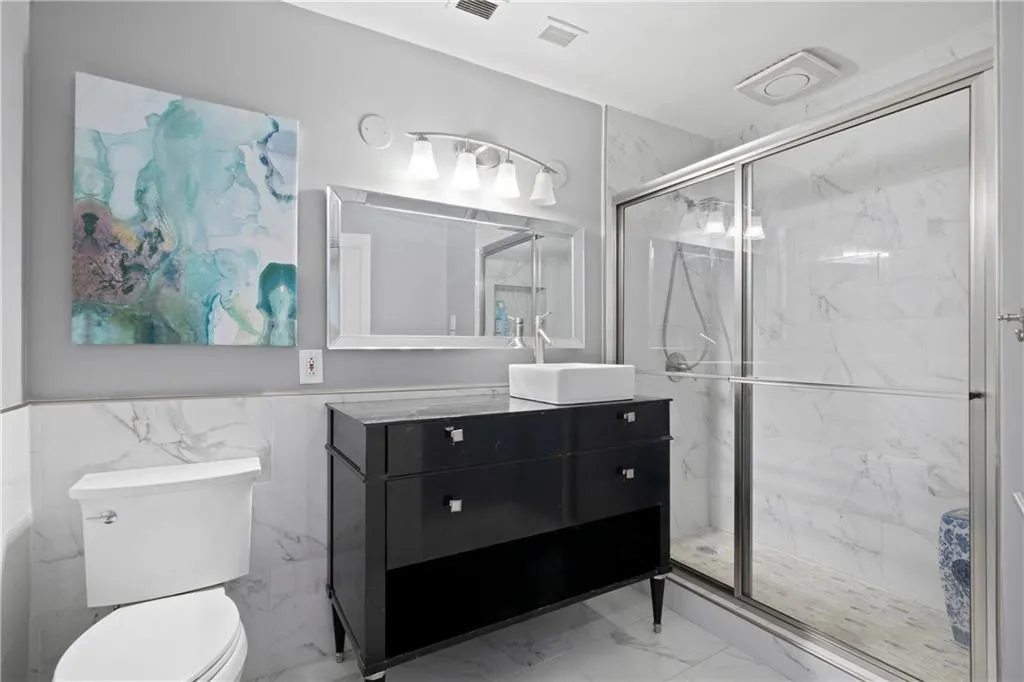 Bathroom with tile walls, vanity, toilet, and an enclosed shower