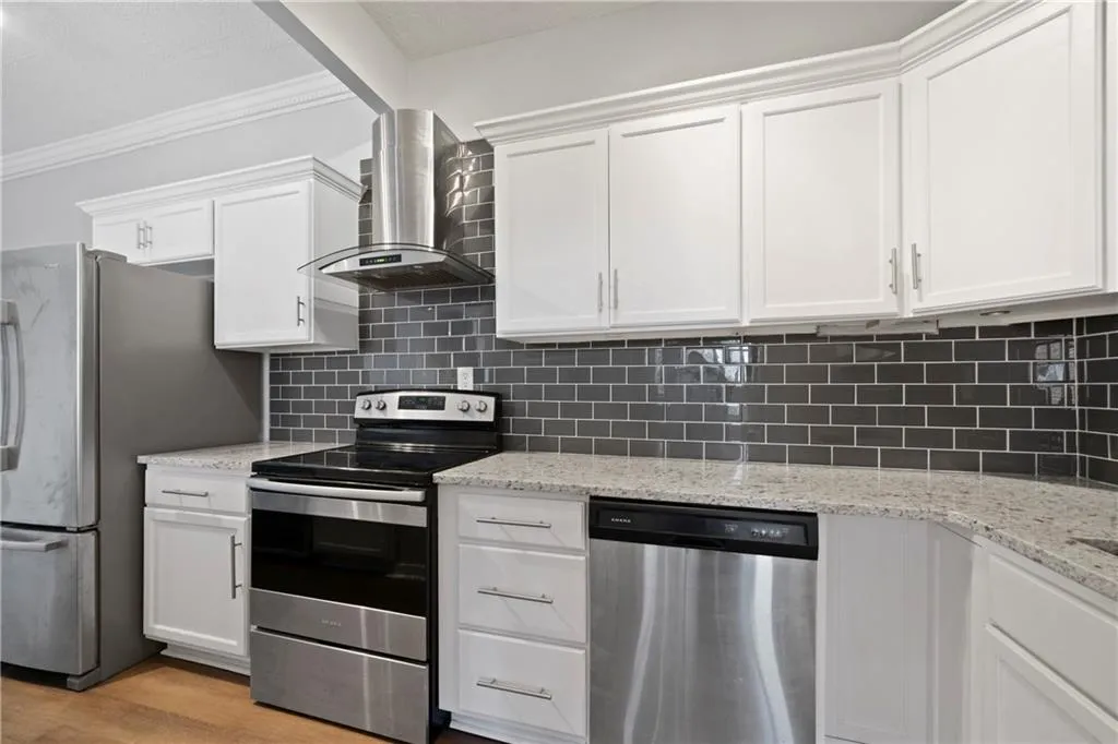Kitchen featuring light wood-type flooring, appliances with stainless steel finishes, wall chimney exhaust hood, and white cabinetry