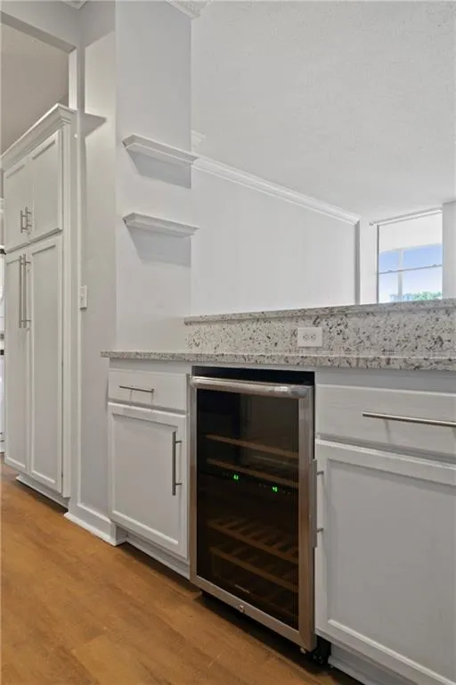 Kitchen featuring white cabinets, wine cooler, light stone countertops, light wood-type flooring, and crown molding