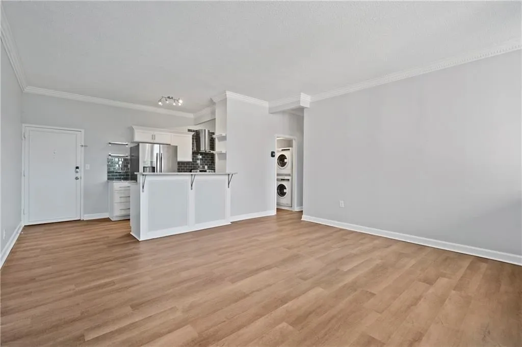 Unfurnished living room with light wood-type flooring, crown molding, and stacked washer and dryer