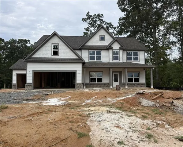 Two-story residence featuring a covered front porch, white siding, stone veneer accents, multiple gable roofs, and attached garages