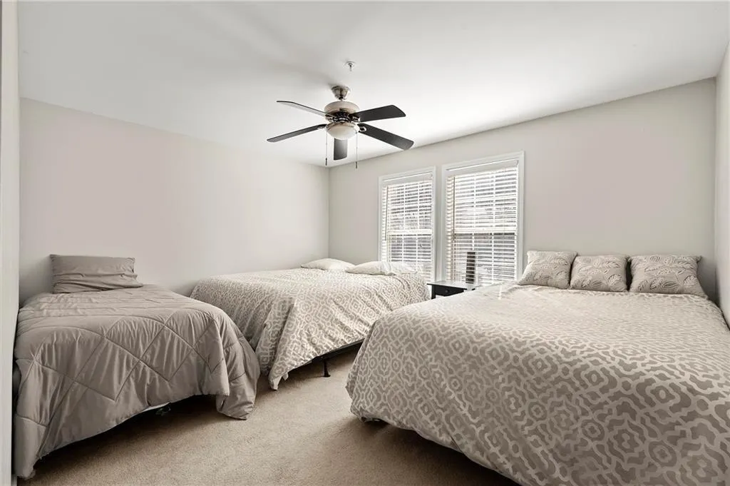 Bedroom featuring light neutral wall paint, two windows with white blinds, a ceiling fan with light fixture, and carpeted flooring