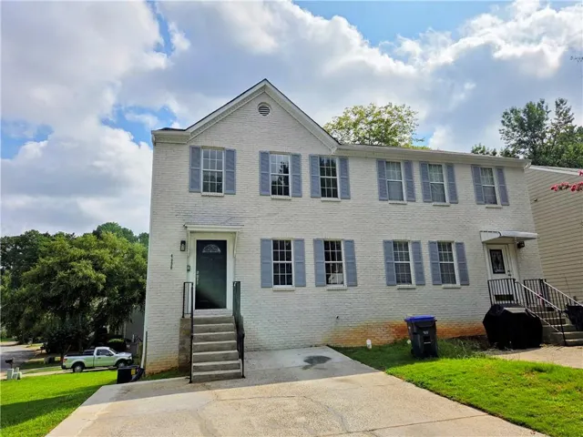 White brick exterior with a gable roofline, light blue shutters, and a front entry door