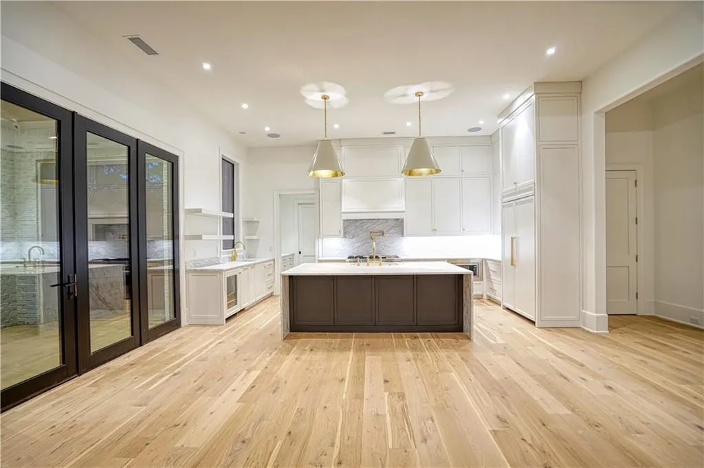 Kitchen with light hardwood / wood-style floors, a kitchen island with sink, pendant lighting, and white cabinets