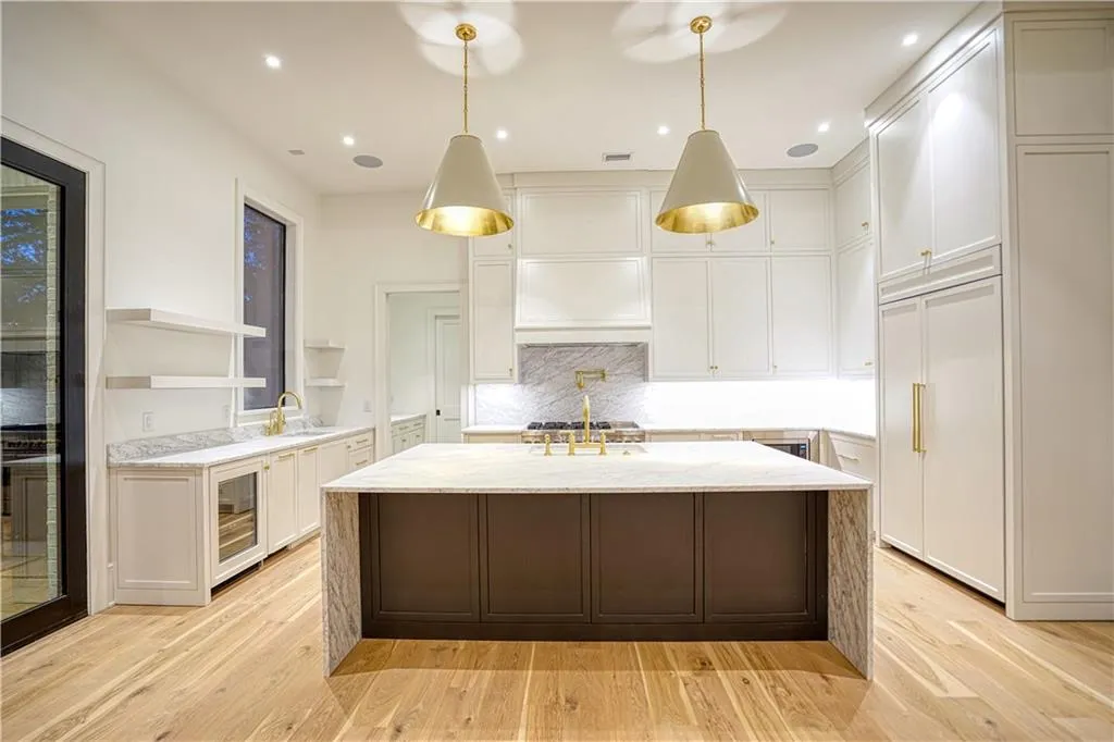 Kitchen with light stone countertops, light wood-type flooring, white cabinets, and decorative light fixtures