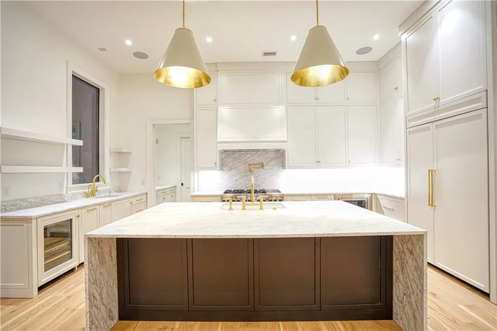 Kitchen with pendant lighting, wine cooler, a kitchen island with sink, white cabinets, and light hardwood / wood-style flooring
