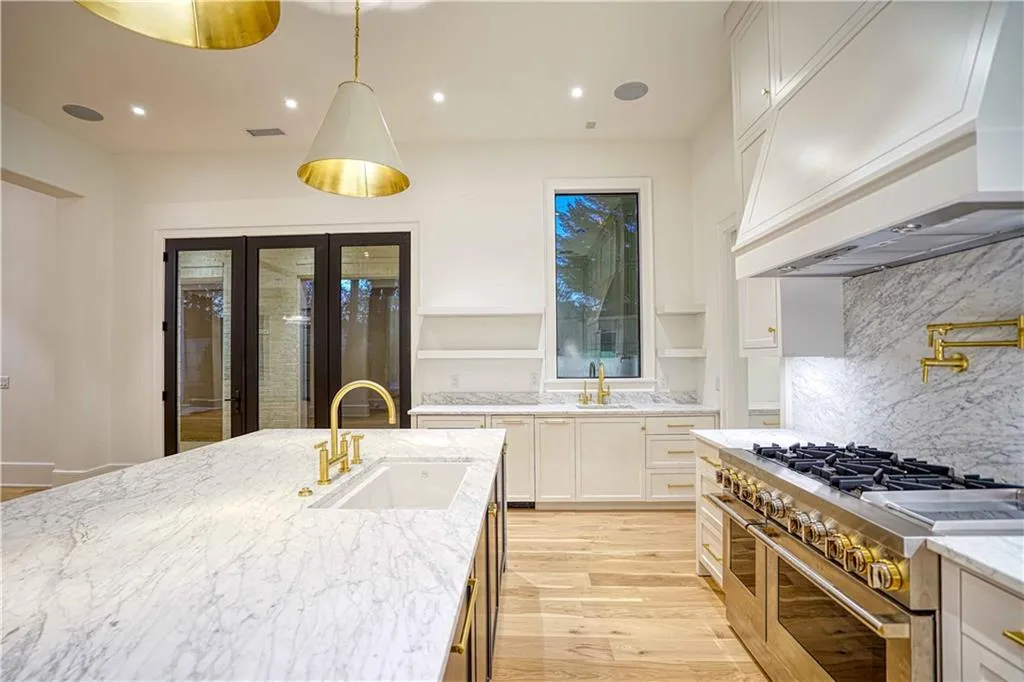 Kitchen featuring custom range hood, white cabinets, light stone countertops, range with two ovens, and sink