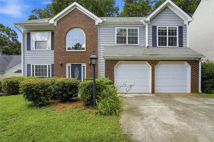 Two-story residence featuring a brick and siding facade, a prominent arched window, a two-car garage, and a concrete driveway