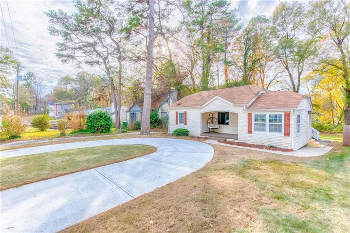 White brick exterior with red shutters, a covered porch, and a concrete circular driveway