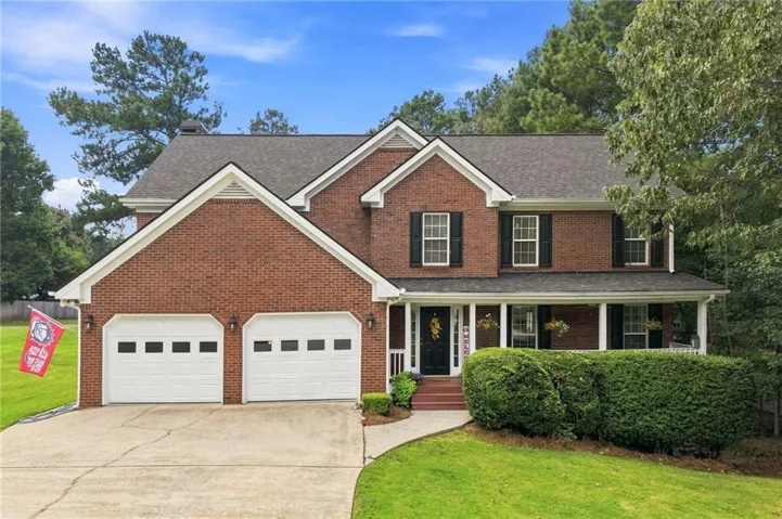 Brick exterior with gabled roof lines, a covered front porch, a two-car garage with white doors, and a paved driveway