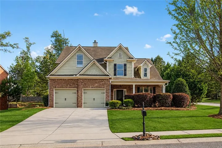 Two-story brick and siding home featuring a dual-car garage, covered front porch, and dormer windows