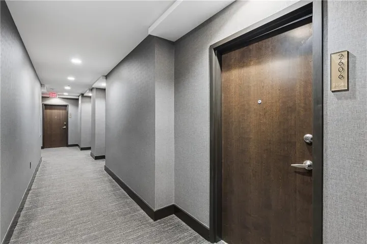 Hallway featuring textured grey wall coverings, recessed ceiling lights, and grey patterned carpet flooring