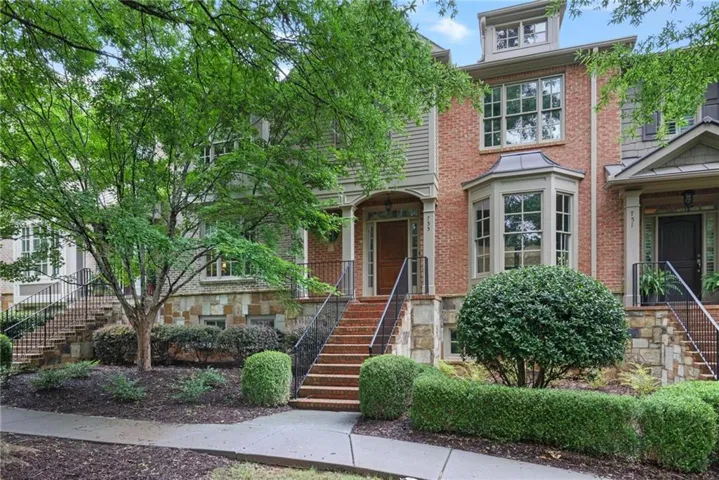 Brick and stone facade townhome featuring a bay window, dormer window, and a welcoming entry with an arched portico
