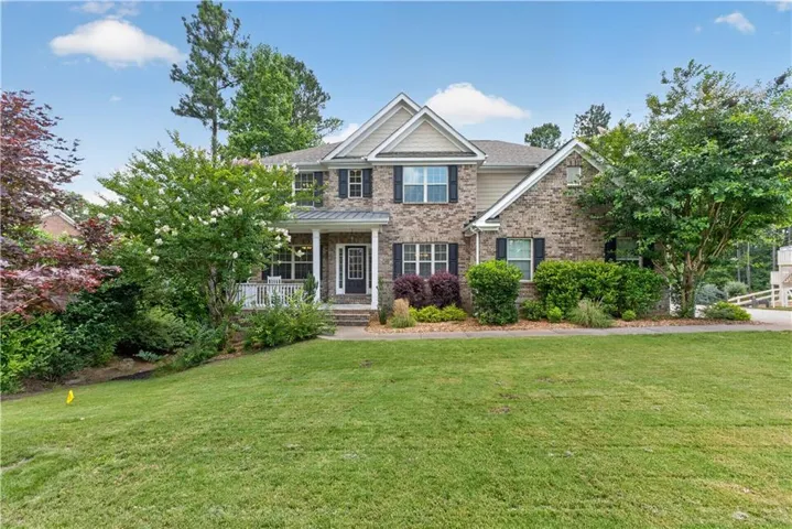 Two-story residence featuring a brick and siding exterior, a covered front porch, and mature landscaping