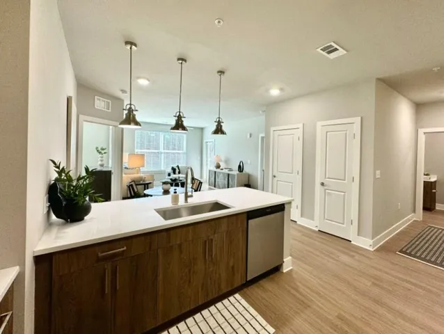 Kitchen with dark brown cabinets, light wood-type flooring, stainless steel dishwasher, hanging light fixtures, and sink