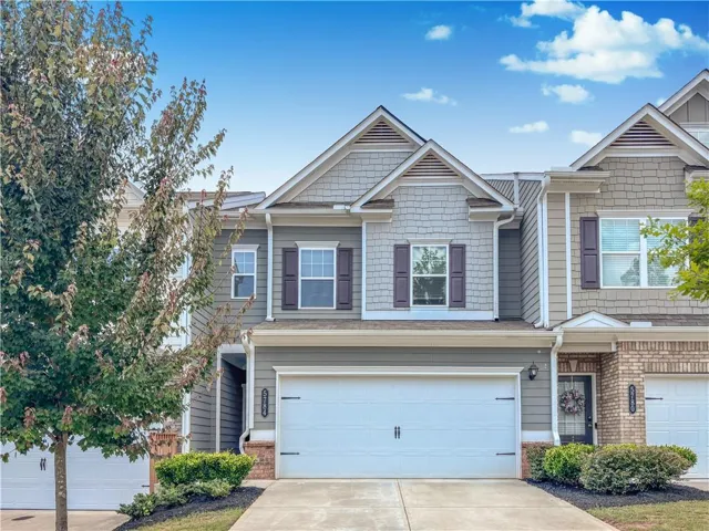 Contemporary townhome exterior featuring a two-car garage, gray siding, shake siding accents, dark shutters, and a covered entry