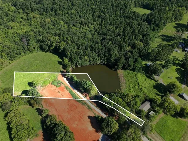 Expansive land parcel featuring a natural pond, wooded areas, and cleared spaces
