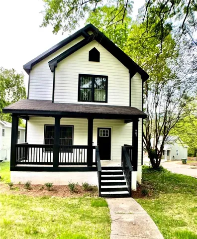 View of front of home with covered porch, a front yard, and a shingled roof