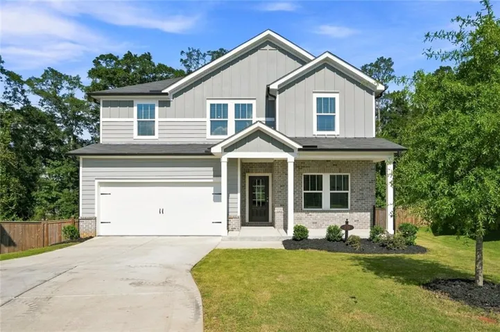Two-story residence featuring a gray siding and brick exterior, attached two-car garage, covered porch entry, and a concrete driveway