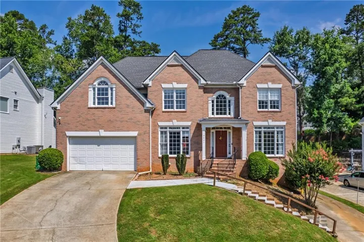Traditional brick facade home featuring a two-car garage, arched entry window, and mature landscaping